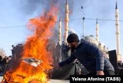 Участники акции протеста против Янгулбаевых на центральной площади Грозного сжигают плакаты с фотографиями членов семьи Абубакара